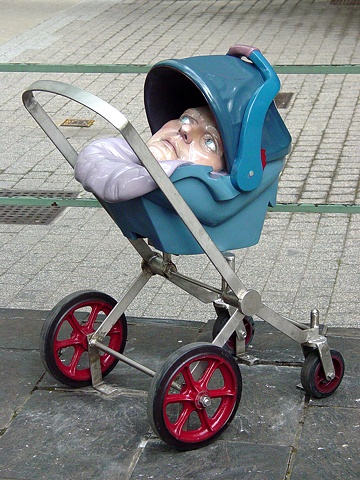 stainless steel stroller holding a car seat which contains an oversized adult head