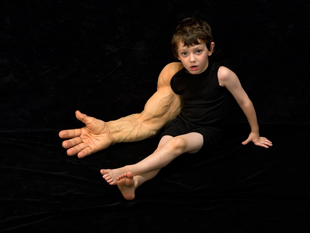 Digital C-Print of small boy sitting on black background with large muscular arm