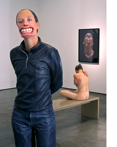 two figurative polychrome sculptures, one of an oversized woman wearing a mask with oversized mouth and lips and the other of a smaller nude woman with oversized glove-like hands