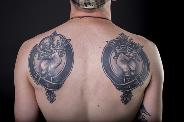 hands holding crown in belts black and grey shoulder piece tattoos