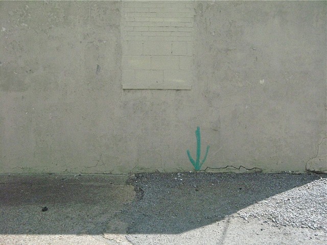 Aqua blue spraypaint points to a crack in the white wall with a bricked-up window in Clarksdale, MS, home of the blues, by Baltimore artist Jo Brown.