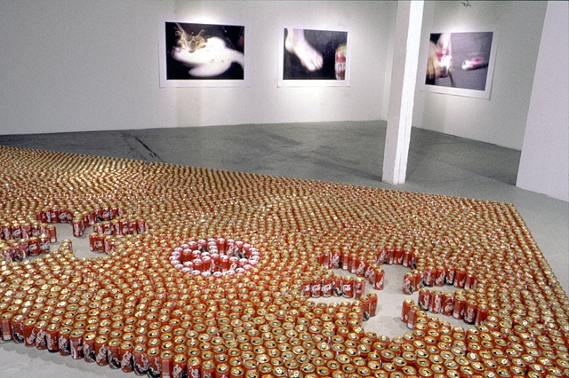 empty coke cans arranged on the floor in a "peace and love" pattern and 3 digital prints captured from video of a coke pour 