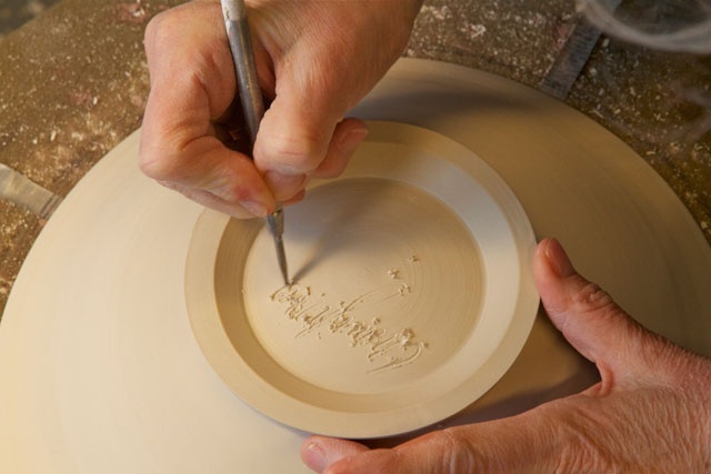 Carol Naughton signing a porcelain bowl after trimming. Firing will be done in a Bailey gas kiln.