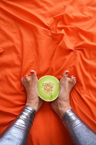 photograph of woman feet legs toes honeydew melon food silver leggings fetish orange bed by Robyn LeRoy-Evans