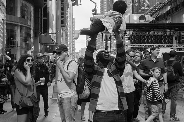 Photograph of a father holding up his child in joy, Times Square, NY, Manhattan, by Judith Ebenstein