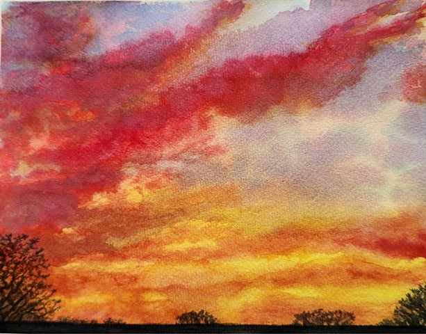 a deep pink and yellow sunset in a deepening blue sky with a dark horizon and trees in the foreground