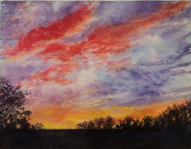 a deep pink and yellow sunset in a deepening blue sky with a dark horizon and trees in the foreground