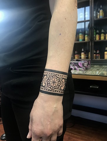 this is a tattoo of an Egyptian inspired ornamental wrist cuff done in a black work style by Amanda Marie tattoo artist and tarot reader in Los Angeles California at her private tattoo studio ace of wands tattoo