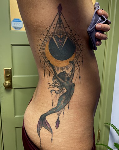 This is a tattoo of a mermaid carrying the moon across the night sky inspired by art nouveau and including ornamental elements as well as spiritual and sacred meaning done by Amanda Marie female tattoo artist and tarot reader in Los Angeles California 