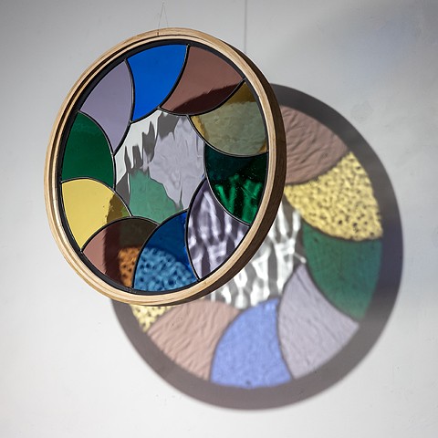 Natalie Hunter %Aperture 02, Light Unfolding (Shades of Dusk)% 2026 Glass, lead, zinc, hand shaped and curved oak, light. 20" round.  Produced with the generous support of the Canada Council for the Arts.