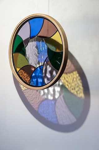 Natalie Hunter %Aperture 02, Light Unfolding (Shades of Dusk)% 2026 Glass, lead, zinc, hand shaped and curved oak, light. 20" round.  Produced with the generous support of the Canada Council for the Arts.