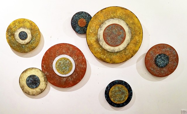 Circular art installation wall sculpture of elevated disk paintings in an earthy palette. 