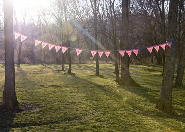 Backlit bunting banner reading, "I'm sorry I let you down" hanging between trees.