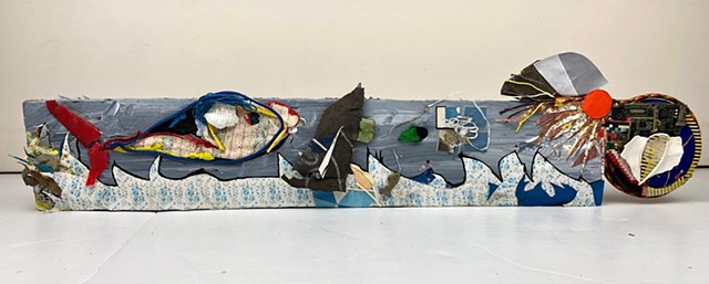A seascape by Steven Tannenbaum, this piece uses Monet-like collage elements along with found objects to depict a fish, boat, and sun in a rocky ocean