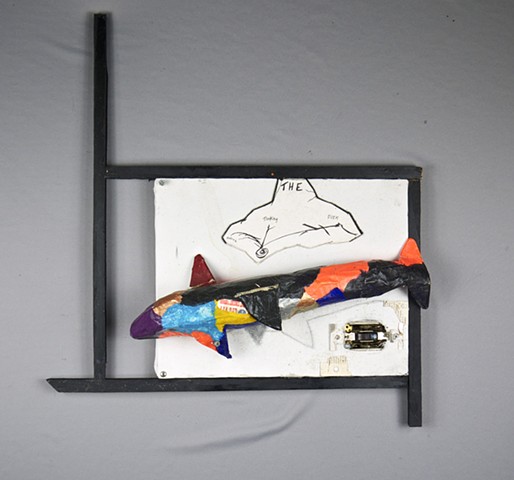 This found object assemblage art piece by Steven Tannenbaum of StructureSlash Modern Assemblage art uses words written in pen, a paper mache shark, and a light switch along with wood to create a square space