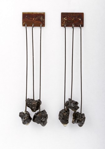 a pair of earrings made of rusted steel, sterling silver, steel wire, asphalt and resin.