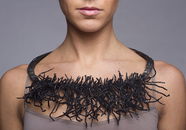 a one-of-a-kind steel wire neckpiece that is composed of welded raw steel wire, black crepe paper, string, lacquer and plastic dip