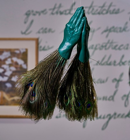 Green praying hands with peacock feathers attached