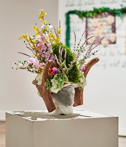 Helmet covered in lush silk foliage, atop a mannequin head, sitting on a pedestal
