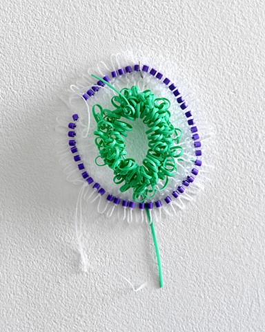 small hand netted sculpture made with craft lacing, nylon, and perler beads by José Santiago Pérez hangs on th gallery wall 30" from the floor