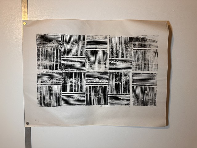 a print hangs on the wall. It's on newsprint and handed printed with black ink. Each section of the print has horizontal lines and vertical lines repeated to make up a larger rectangle pattern.