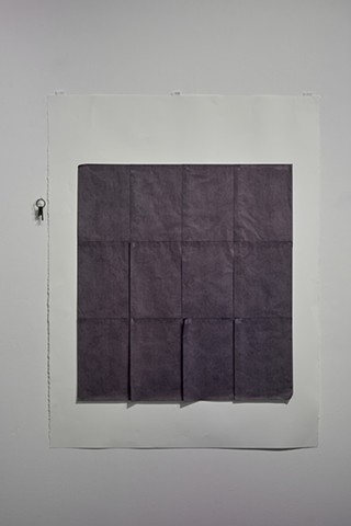 smaller sheets of black carbon paper are in rows as a larger sheet, four across and three down. This is hung in the center of a larger white sheet of paper. To the left hangs of set of old keys.