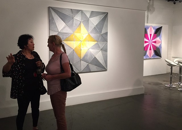 Artist Chun Hui Pak discusses her art with the first visitor to the opening