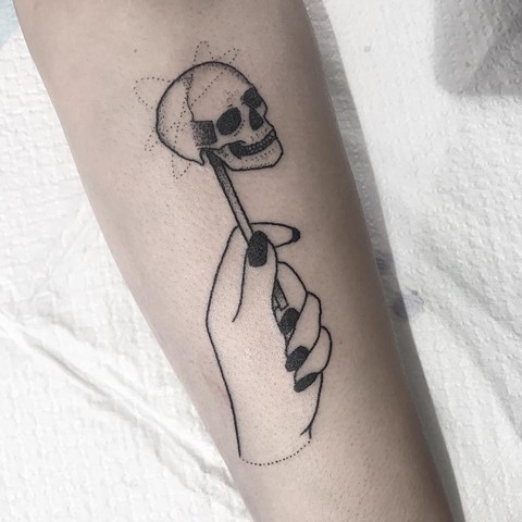 Skull lollipop held in the hand. Black ink tattooing by Amy Jones. Located in Coburg, Melbourne, Victoria. Melbourne tattoo and art studio, Australia. Professional Stick and poke tattooing