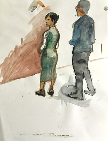 Two standing figures looking at art; one, a woman, wears a green dress.