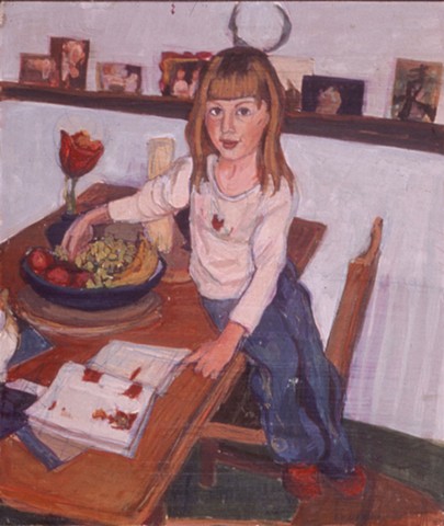 A young girl sits on a table pointing to a book and an apple.