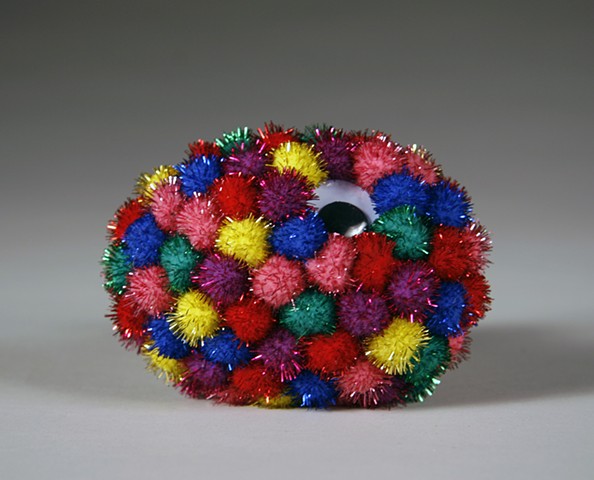 found rock sculpture covered in one large wiggle eye and rainbow shiny pom poms by Holly Campbell