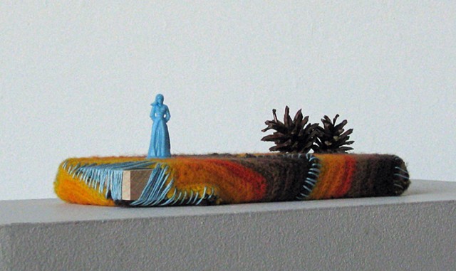 plastic toy figure, pine cones with yarn and embroidery thread on wood by Holly Campbell