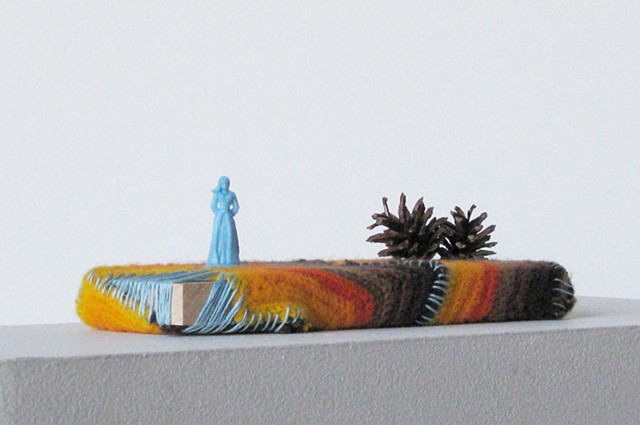 plastic toy figure, pine cones with yarn and embroidery thread on wood by Holly Campbell