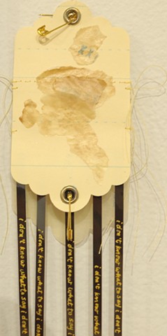 I Don't Know What To Say--detail of "funnel" wall tag, "XX", coffee-stained waxed paper layers, sewn sentence strips, safety pins, gold ink writing on audio cassette strands