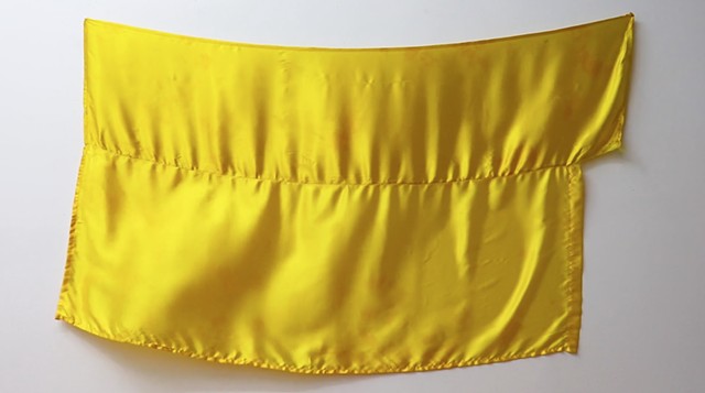 Image Description: Two horizontal gold synthetic fabric panels sewn together at a midpoint to create a flag structure. The fabric panels have some discoloration, stains, wear and tear from use. The flag is pinned at the right and left top corners onto a w