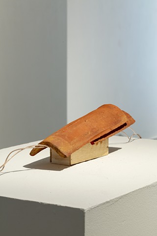 Two roof tiles on top of a wooden block on a white pedestal with wires coming out on each side.