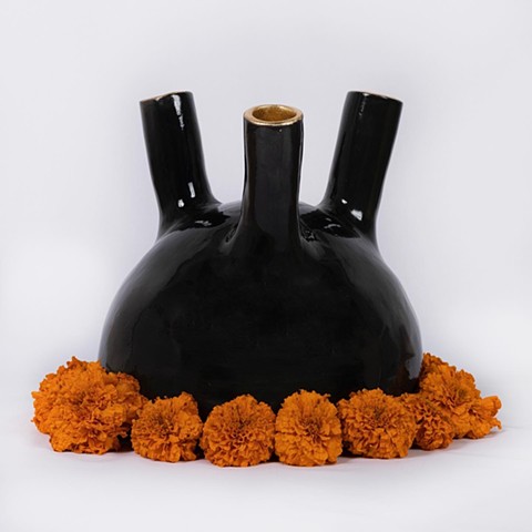 Black Ceramic Vessel half sphere with three spouts pointing to the sky with gold leafed rims surrounding the bottom are large luscious orange marigold flowers
