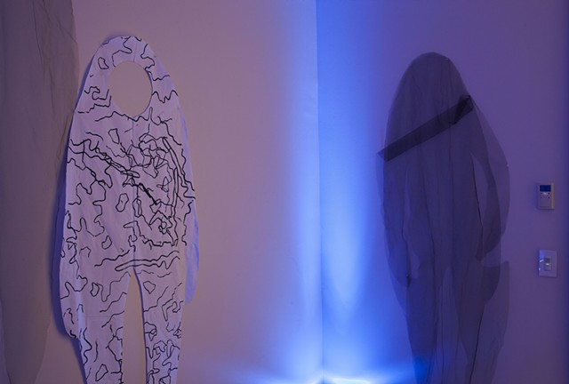 two cloth figures are pinned to the walls of a room illuminated by blue lights