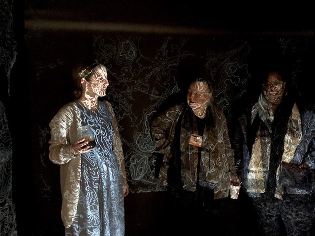 three people stand in front of a black wall with squiggly white lines projected on them