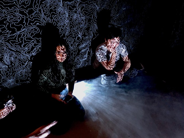 two people sit in front of a black wall with squiggly white lines projected on them