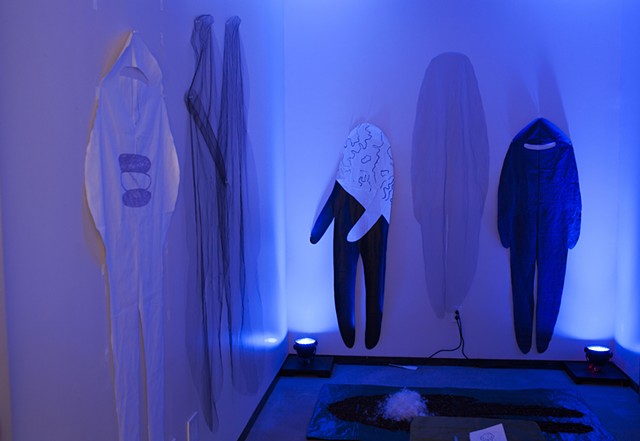 six cloth figures are pinned to the walls of a room illuminated by blue lights