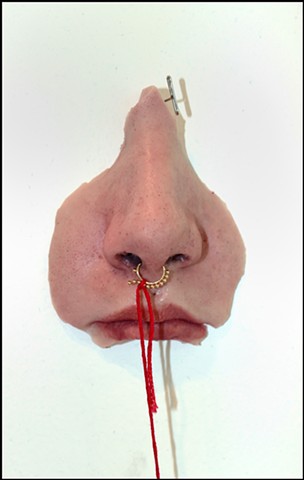 Silicone nose sinking into the wall, tethered by a cotton thread and attached zine on the nose piercing.