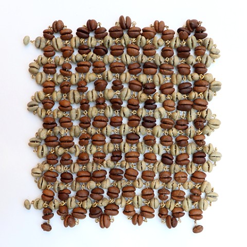 A mesh-like almost square made from a chain of green unroasted coffee beans woven like a fabric over and under through another chain of brown roasted coffee beans. The beans fit together in pairs and are connected by tiny loops of golden brass that go through the center of the beans like beads. 