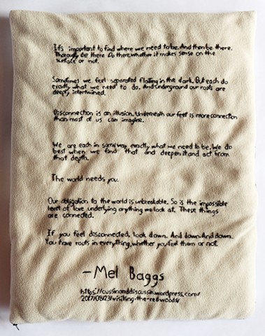 This side of the lap pad is a light sand color soft fleece. The lap pad is a vertical rectangle and a couple inches thick. A quote is hand embroidered with black embroidery floss. Each sentence of two is separated by a break. Mel Baggs’ name is embroidere