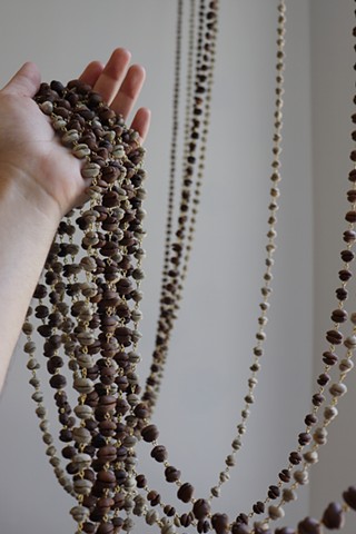 Chains of alternating green unroasted and brown roasted coffee beans gloriously cascade off of my hand, palm opened, as I gather them together and lift them up. The prayer bead like chains of coffee, delicately linked by golden brass, trail behind and above my hand, installed like a beaded curtain along a window beyond the image frame. 