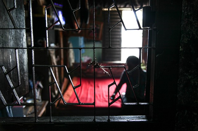 A sex worker's next customer quietly waits on her bed in the Rathkhola Brothel in Faridpur, Bangladesh. 
