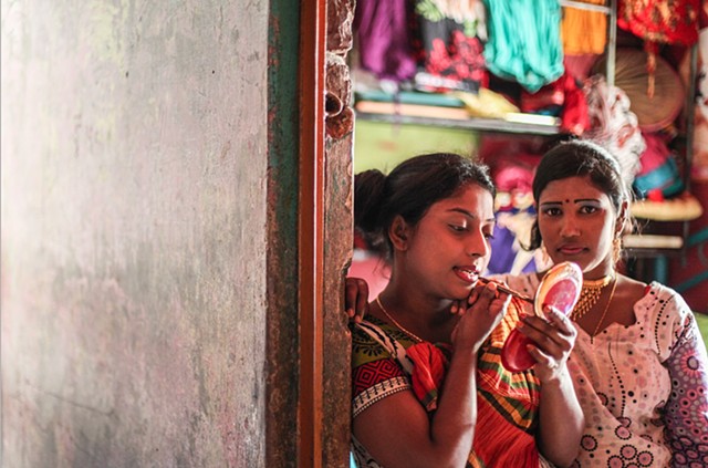 A sex worker in the Rathkhola Brothel in Faridpur, Bangladesh fixes her makeup as her friend looks on. Men selling makeup periodically walk through these brothels, allowing the young sex workers to prepare for incoming customers.