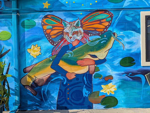 Iowa city bike library mural of a woman with a bobcat head and butterfly wings holding a giant flathead catfish