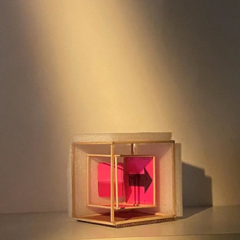 A sculpture of a cube with the two back sides enclosed with foam. The interior houses a red paper with an arrow pointing right drawn on it.