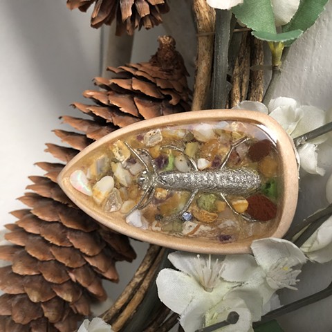 Pewter caddisfly set in hand-carved maple with beach agates and an Idaho opal by Ryan C Sedgeley.